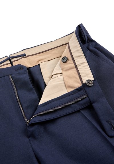 Un pantalon bleu marine doté d'une braguette zippée et de deux boutons noirs, avec une doublure beige contrastante et une couture accentuée marron le long de la ceinture.