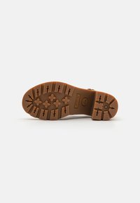 Brun gummistøvelsåle med et mønster av dekk. Har et Timberland-logo og flere friksjonselementer for grep og stabilitet.