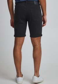 Black denim shorts with rolled cuffs, five-pocket design, and a leather label on the back. White sneakers complete the outfit.