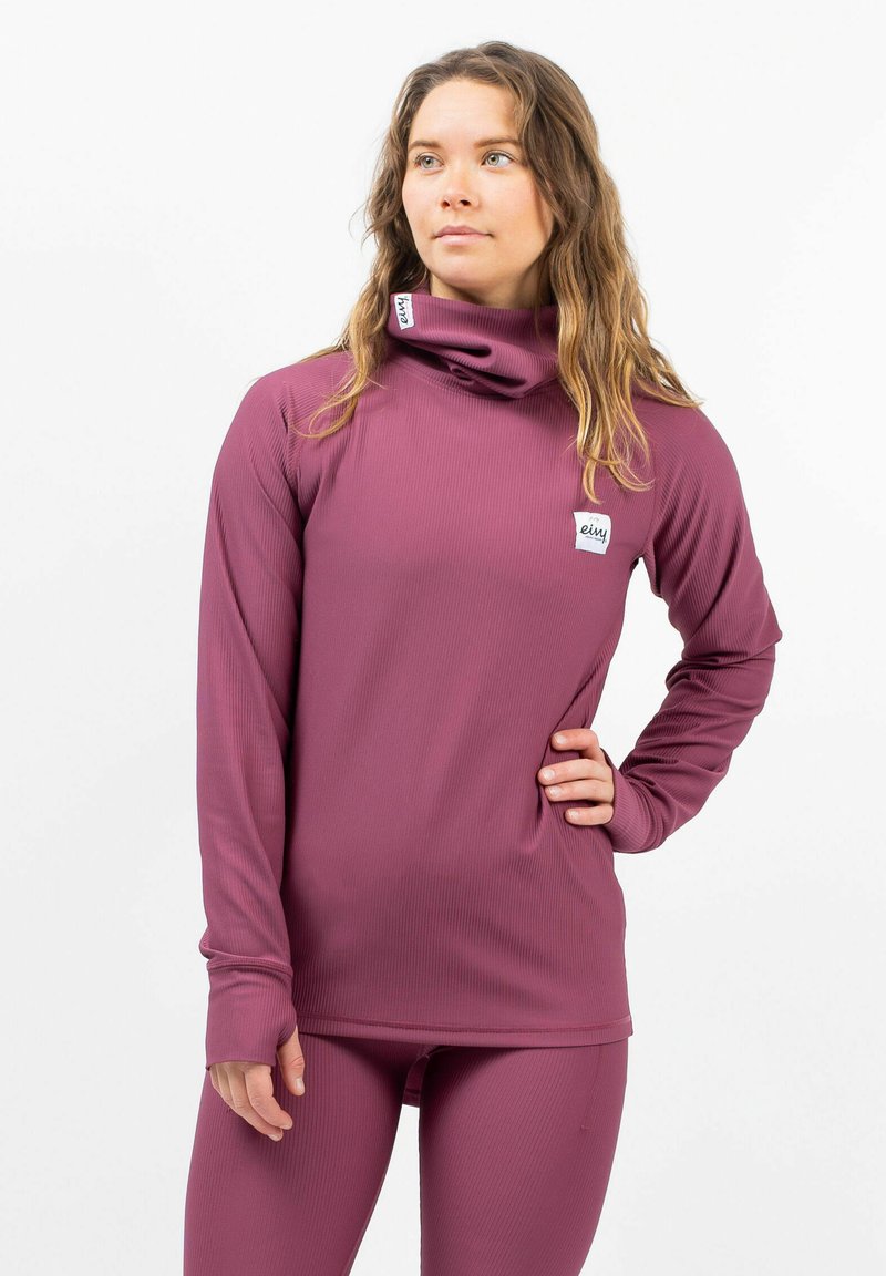 Long-sleeved, purple thermal top with a high collar, ribbed texture, and logo tag on the chest. Styled with matching fitted pants.