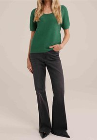 Haut court à col arrondi de couleur verte texturée, associé à un jean flare sombre et des chaussures noires pointues, créant une tenue décontractée.