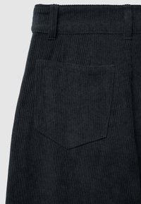 I pantaloni di velluto a coste neri presentano una texture a righe verticali, una vita con passanti per la cintura e una tasca posteriore con un cappuccio puntato.
