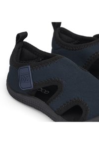 Slip-on-skor i marinblått tyg med svarta detaljer, öppna sidor, texturerad gummisula och liten präglad logotyp. Lätt och flexibel design.