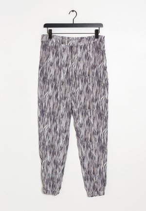 Luźne spodnie z abstrakcyjnym szaro-białym wzorem przypominającym pióra, elastyczną talią i mankietami przy kostkach, wiszące na czarnym wieszaku.