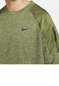 Homme portant un t-shirt à manches longues vert chiné avec des panneaux en tissu vert olive et un logo Nike swoosh noir sur la poitrine.
