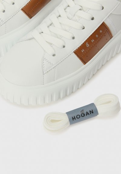 Baskets en cuir blanc avec une accent en cuir marron, dotées de lacets plats, de coutures contrastées et d'une semelle épaisse à rainures. Comprend des lacets blancs supplémentaires.