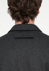 Szürke gyapjúkabát kitűnő gallérral, hátul hasítékkal és "HUGO" márkajelzéssel a gallér felett. A textúra puha és sima hatású.