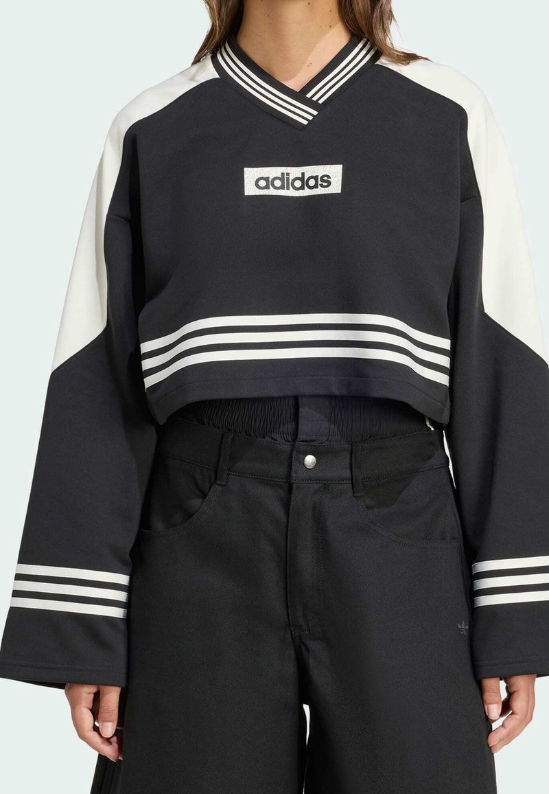 Černobílá zkrácená mikina s výstřihem do V, s logem Adidas, širokými rukávy a bílými pruhy na lemu a rukávech.