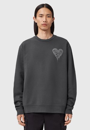 Sweatshirt gris foncé avec un col rond, des manches longues et un graphique en forme de cœur sur la poitrine. Texture douce et coupe décontractée.