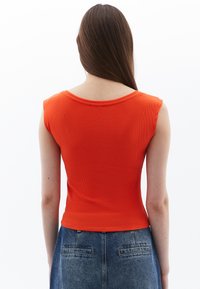 Top a righe rosso con maniche a campana, caratterizzato da un collo rotondo e una silhouette aderente, abbinato a una gonna in denim a vita alta.