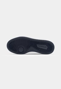 Sole delle sneaker Lacoste in gomma blu scuro, con un motivo a spina di pesce per la trazione e una sezione circolare con il logo del marchio.