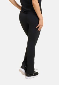Leggings neri con un design aderente, caratterizzati da una texture liscia e una leggera svasatura all'orlo, abbinati a scarpe nere con suole bianche.