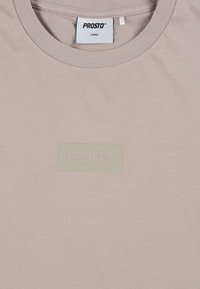 Jasnokremowa koszulka z miękkiej bawełny, z teksturowanym, przezroczystym logo "PROSTO" na prostokątnym wszywce. Okrągły dekolt.