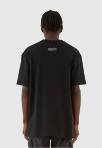 Sort bomulds T-shirt med afslappet pasform, der har korte ærmer og et diskret logo i grå på den øverste del af ryggen.