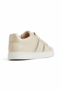 Sneakers sintetici beige con una striscia di rilievo testurizzato e accenti di strass sul lato, suola in gomma bianca e supporto posteriore imbottito.