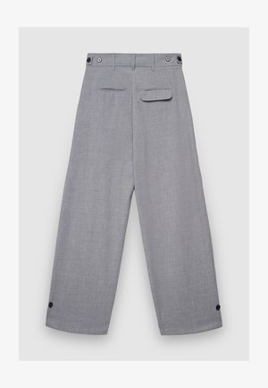 Pantalon large couleur gris clair en tissu texturé, doté de deux poches arrière, de fermetures à boutons sur le devant, et de boutons-pression aux poignets.