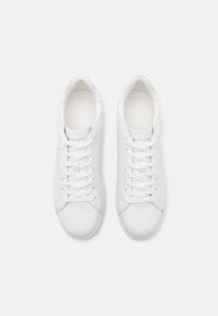 Hvit lær sneakers med lavt design, snøring foran og preget logo på tungen. Glatt tekstur, minimalistisk stil.