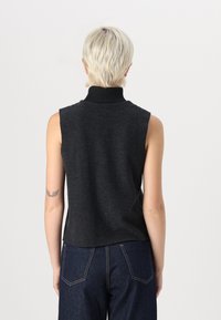 Tamno siva bezrukavna turtleneck majica od mekog materijala s rebrastim ovratnikom. Uparena s tamnoplavim farmerkama visokog struka.