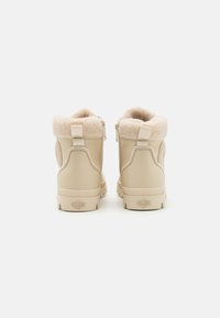 Bottines beiges avec une douce doublure en fausse fourrure, fermeture éclair latérale et semelle en caoutchouc texturé, dotées d'un logo sur le talon et d'une boucle à l'arrière pour un enfilage facile.