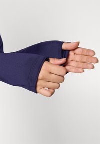 Navy long-sleeve top with thumbholes, featuring a smooth, stretchy fabric. Close-up of hands holding the cuff, showcasing soft texture and fit.