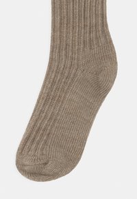 Braune gerippte Socke mit weicher Textur, versehen mit verstärktem Fersen- und Zehenbereich für mehr Haltbarkeit. Die Socke reicht in der Länge bis zur Mitte der Wade.