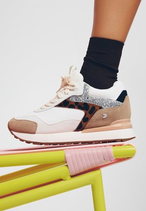 Sneaker sportivo con una tomaia bianca, pannello a stampa leopardata, accenti luccicanti e dettagli in suede beige. Posato su una superficie flessibile, rosa e gialla.