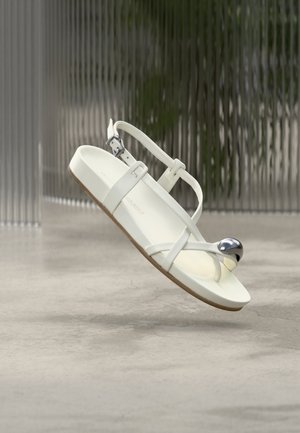 Hvit sandal laget av glanset materiale med tynne stropper, justerbar spenne og en dekorativ metallisk kule på tåen. Lett design.