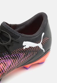 Musta jalkapallo, jossa on teksturoitu yläosa, valkoisella logolla, oranssista purppuraan gradienttiväriin siirtyvät korostukset ja kontrastinen oranssi pohja.