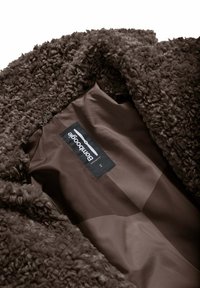 Cappotto in finta pelliccia riccia marrone con una superficie interna liscia, dotato di etichetta del marchio Bomboogie e tag di taglia 2.