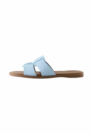 Sandale à glissière en suédine bleue avec un design de brides entrecroisées et une semelle plate en caoutchouc brun. Texture lisse sans motifs visibles.