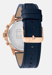 Montre avec bracelet en cuir bleu marine, boîtier en acier inoxydable rose gold, cadran rond et fermoir à boucle. Présente un dos lisse avec des détails de logo.