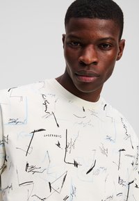 Hvid bomuld t-shirt med abstrakte sorte og lyseblå skitser, rund crew neck og korte ærmer. Brand logo synlig.