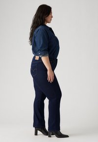 Mörkblå denimjeans med en åtsittande form, med en hjärtformad baks pockets design, tillsammans med en mörk denimskjorta och svarta klackstövlar.