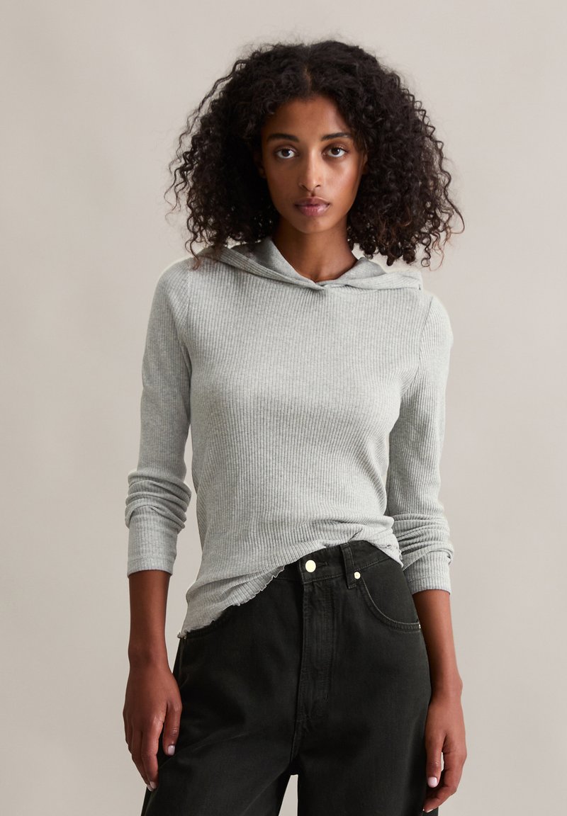 Grijze geribde sweatshirt met een trekkoord en lange mouwen, gecombineerd met zwarte high-waisted jeans, met een relaxed fit en minimale details.