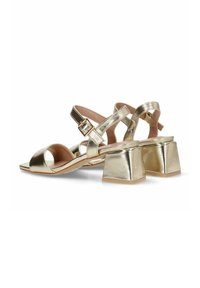 Sandalias metálicas doradas con diseño de punta abierta, correa ajustable en el tobillo y tacones de bloque grueso. Parte superior texturizada y detalles de estilo minimalista.