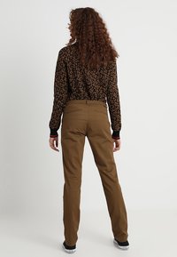 Pantalons marron avec une coupe droite. Le matériau semble solide, avec une texture lisse. Pas de matériel ni de motifs visibles. Design simple et intemporel.