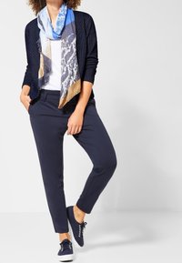 Námořnický kardigan s puntíky, bílá košile, námořnické kalhoty a šátek s modrým vzorem, doplněný námořnickými teniskami, neformální souprava.