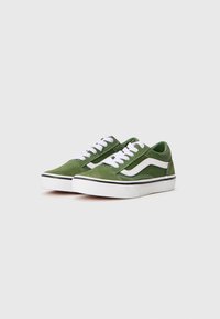 Une paire de baskets basses en suède vert avec une rayure blanche sur le côté, des lacets blancs et des semelles en caoutchouc blanches sur un fond clair.