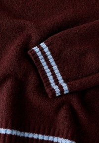 Bordeauxfärgad stickad tröja med en mjuk textur, med blåa och vita randiga detaljer på ärmsluten och nederkanten.
