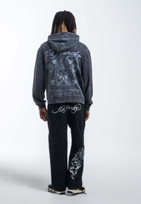 Sudadera negra con diseños gráficos en la espalda, que presenta una calavera y llamas. Combinada con pantalones negros que exhiben un estampado floral.