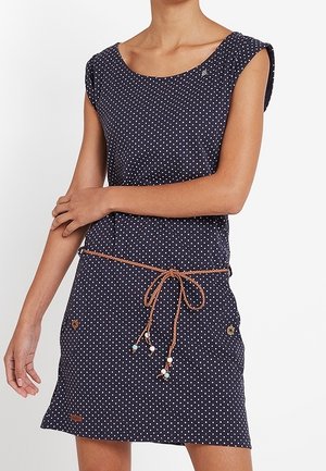 Mouwloze marineblauwe jurk met witte polka dots. Voorzien van een taillekoord met kleurrijke kralen en twee voorzakken met knoopdetails.