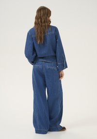 Denim outfit featuring a loose-fitting jacket and wide-leg pants in a medium blue shade, highlighting stitching details and relaxed silhouette.