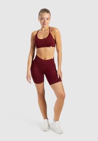 Bordeaux sportbeha en hoge taille shorts gemaakt van rekbare stof. Heeft een aansluitend ontwerp met zichtbare naden. Gedragen met witte sneakers.