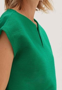 Zelený žebrovaný top s kulatým výstřihem a krátkými rukávy, s jemnou vertikální strukturou a detailem s předním rozparkem.