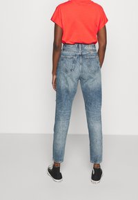 Höga blå denimjeans med ljus tvätt, med avslappnad passform, bakfickor och lätt blekning. Matchas med svarta skor.