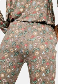 Hnedá tkanina s hravým vzorom húb, kvetov, dúh a symbolov mieru v červených, zelených, žltých a modrých tónoch.