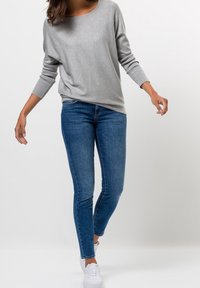 Grå långärmad topp med rund halsringning, i kombination med blå skinny jeans och vita sneakers. Slät tyg med en något lös passform.