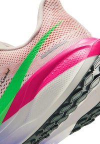 Różowy, siateczkowy but do biegania z jaskrawozielonym logo, różowo-białą podeszwą i czarnym bieżnikiem z wzorem, widziany od strony pięty.