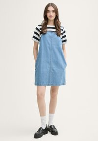 Leren spijkerbroek jurk in lichtblauw met twee zijzakken, gecombineerd met een zwart-wit gestreept shirt met korte mouwen en zwarte platte loafers.