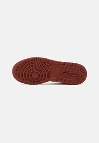 Talpa de adidași roșii din cauciuc, cu modele de tracțiune circulare și liniare, având un token circular central și logoul "Nike" embosat pe latură.